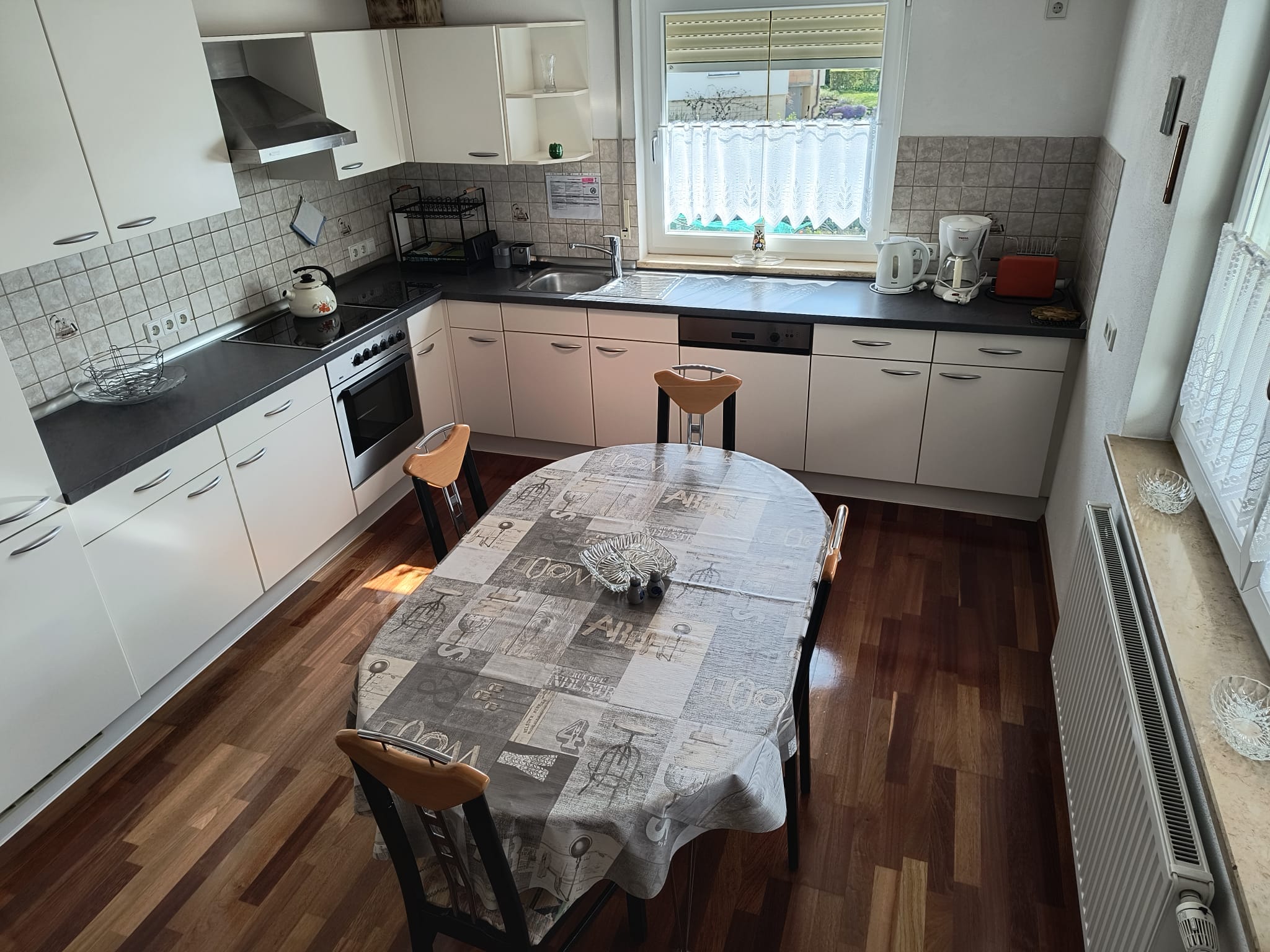 Wohnküche mit Essbereich, Herd, Backofen, Kühlschrank, Kaffeemaschine, Geschirr, Besteck und Esstisch